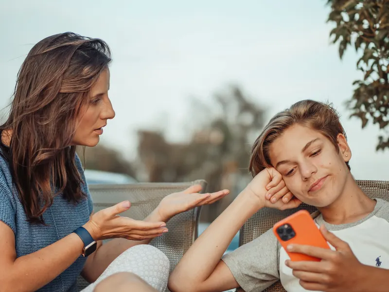 A parent talking with her teenager, who is looking at a phone.